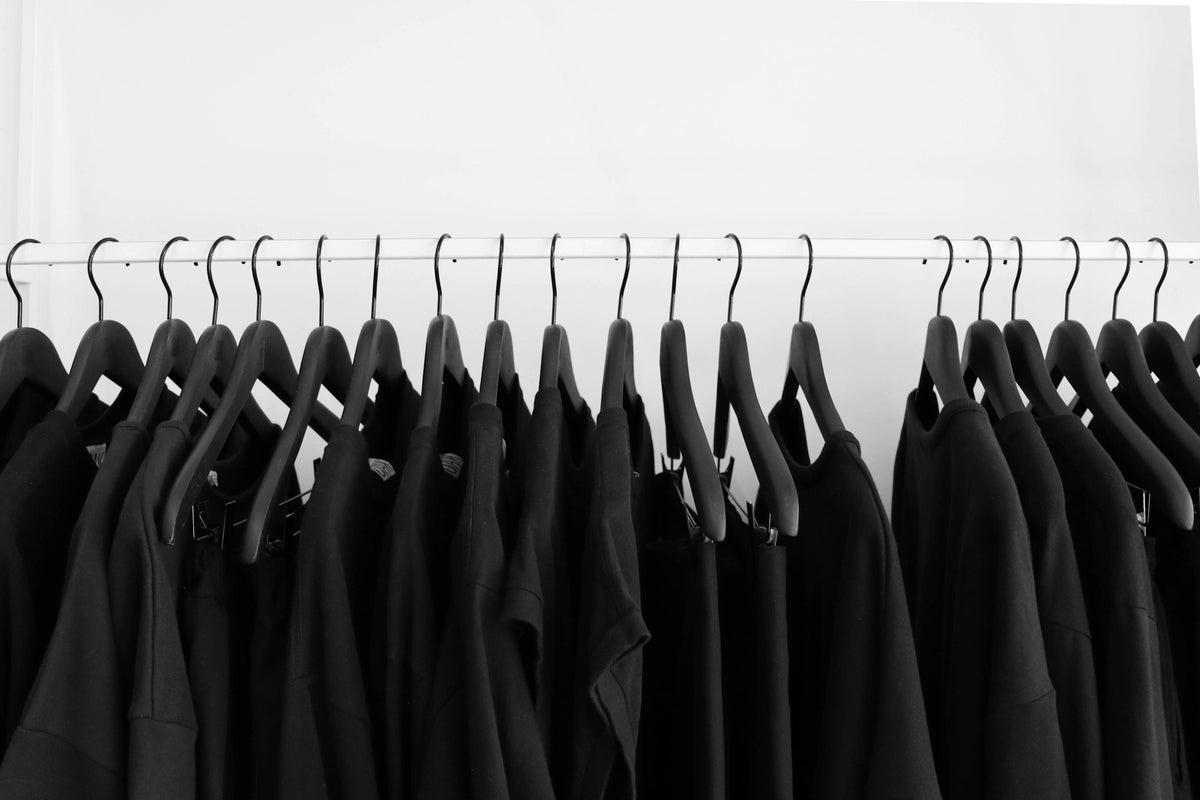 black tees and hoodies hanging on a rail against a white wall
